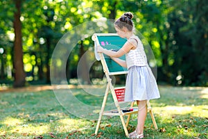 Happy little kid girl standing by big chalk desk Preschool or schoolkid on first day of elementary class. Back to school