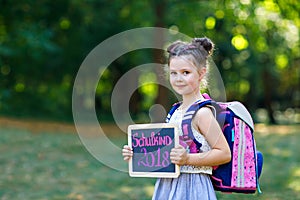 Happy little kid girl standing with desk and backpack or satchel. Schoolkid on first day of elementary class. Healthy