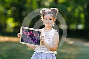 Happy little kid girl standing with desk and backpack or satchel. Schoolkid on first day of elementary class. Healthy