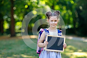 Happy little kid girl standing with desk and backpack or satchel. Schoolkid on first day of elementary class. Healthy