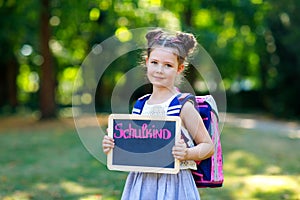 Happy little kid girl standing with desk and backpack or satchel. Schoolkid on first day of elementary class. Healthy