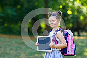 Happy little kid girl standing with desk and backpack or satchel. Schoolkid on first day of elementary class. Healthy