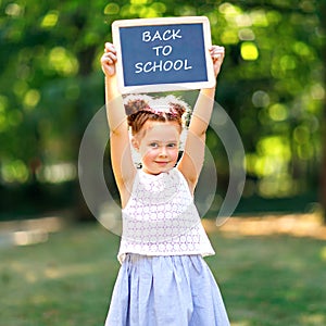 Happy little kid girl standing with desk and backpack or satchel. Schoolkid on first day of elementary class. Healthy