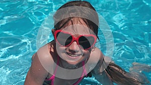 Happy little kid girl in sunglasses in pool on summer sunny day. Childhood fun