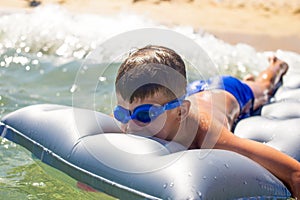 Happy little kid in goggles lying on air water mattress in sea