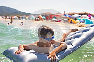 Happy little kid lying on air water mattress in sea on beach