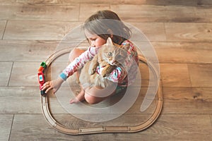 Happy little kid play with toy wooden train railway at home together with pet cat. Toys for children in kindergarten and