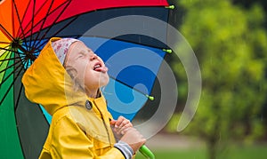 Happy little kid playing outdoors. Little girl hiding behind colorful umbrella outdoors. Rain weather