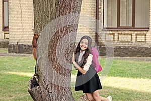 Happy little kid in school uniform with backpack observe squirrel climbing tree in park, outdoor education