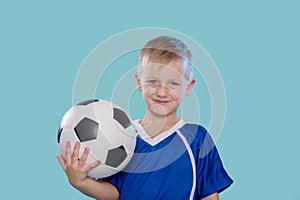 Happy little kid in sportswear holding a soccer ball isolated on blue background