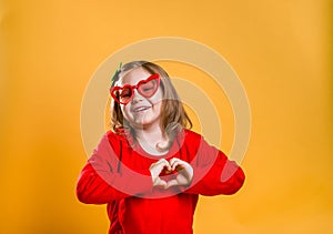 Happy little kid on valentines day. Funny girl make heart from hands isolated on yellow background. Stylish child in red