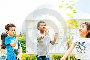 Happy little kids blowing soap bubbles in summer park. Kid and friends in international preschool play a bubble.