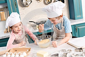 happy little kids in chef hats and aprons whisking dough