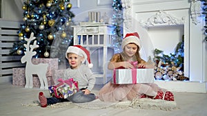 Happy little kids opening presents on Xmas eve. Children under Christmas tree with gift boxes. Decorated living room with