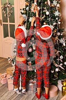 Happy little kids in pajamas decorate Christmas tree in beautiful living room