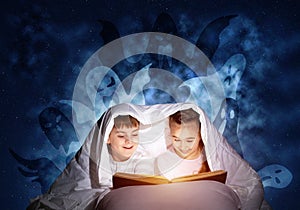 Happy little kids reading book in bed