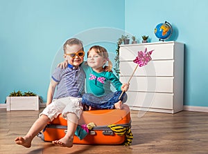 Happy little kids sitting on colorful orange suitcase prepared for family summer vacation. Young travelers. Little girl