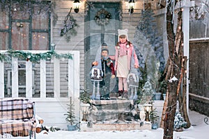 Happy little kids sitting on the porch of the Christmas decorated house outdoor