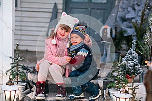 Happy little kids sitting on the porch of the Christmas decorated house outdoor