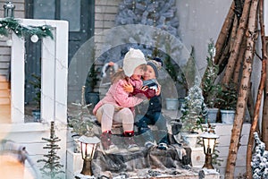 Happy little kids sitting on the porch of the Christmas decorated house outdoor