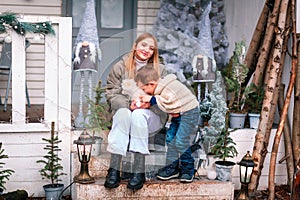 Happy little kids sitting on the porch of the Christmas decorated house outdoor