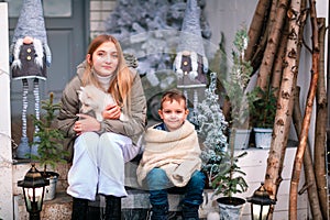 Happy little kids sitting on the porch of the Christmas decorated house outdoor