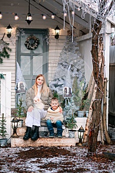 Happy little kids sitting on the porch of the Christmas decorated house outdoor