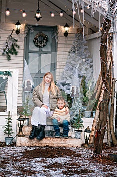 Happy little kids sitting on the porch of the Christmas decorated house outdoor