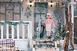 Happy little kids sitting on the porch of the Christmas decorated house outdoor