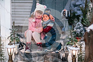 Happy little kids sitting on the porch of the Christmas decorated house outdoor