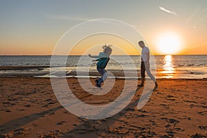 Happy little laughing girl 7 years jumping on the beach playing with dad at sunset