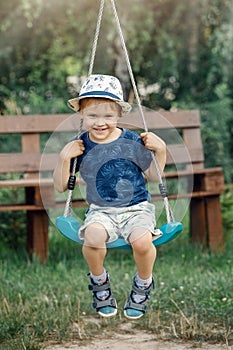 Happy little preschool boy having fun on swing in domestic garden. Healthy toddler child swinging on sunny summer day. Children