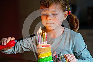 Happy little preschool girl celebrating birthday. Cute smiling child with homemade rainbow cake, indoor. Happy healthy toddler