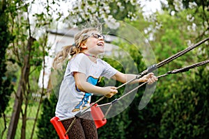 Happy little preschool girl with glasses having fun on swing in domestic garden. Cute healthy child swinging under