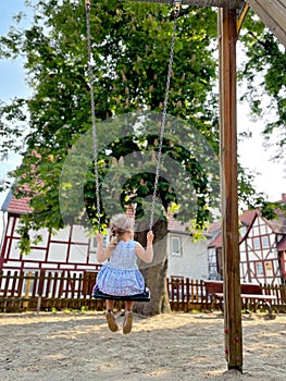 Happy little preschool girl having fun on swing on city outdoor playground. Healthy toddler child swinging on sunny