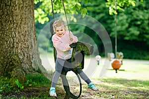 Happy little preschool girl having fun on swing in domestic garden. Healthy toddler child swinging on summer day