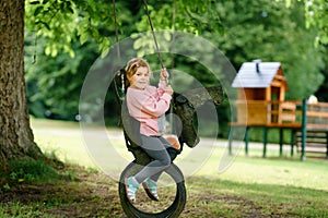 Happy little preschool girl having fun on swing in domestic garden. Healthy toddler child swinging on summer day