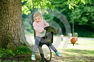 Happy little preschool girl having fun on swing in domestic garden. Healthy toddler child swinging on summer day. Children