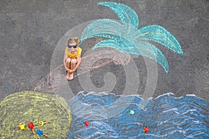 Happy little preschool girl in swimsuit with sea, sand, palm painted with colorful chalks on asphalt. Cute child with