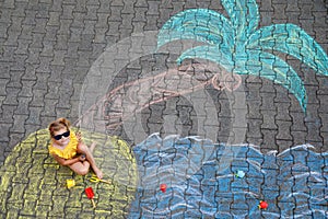 Happy little preschool girl in swimsuit with sea, sand, palm painted with colorful chalks on asphalt. Cute child with