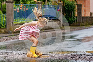 Happy little preschool girl wearing yellow rain boots and walking during puddles. Cute child in colorful clothes jumping