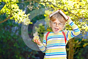 Happy little preschool kid boy with glasses, books, apple and backpack on his first day to school or nursery. Funny