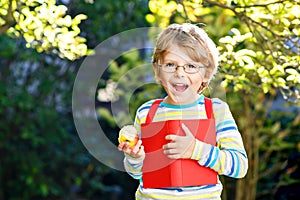 Happy little preschool kid boy with glasses, books, apple and backpack on his first day to school or nursery. Funny