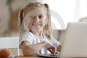 Happy little preschool kid sitting at table with computer.