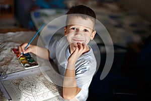 Happy little preschooler boy painting coloring book