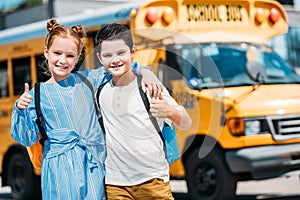 happy little scholars showing thumbs up and looking at camera in front of