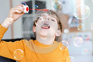 Happy little school boy playing with soap bubbles at home. Kid having fun. Child playing at school, making experiment