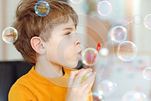 Happy little school boy playing with soap bubbles at home. Kid having fun. Child playing at school, making experiment