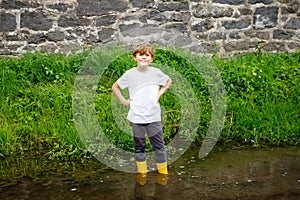 Happy little school kids boy having fun walking through water in river in gum rubber boots. child portrait of healthy