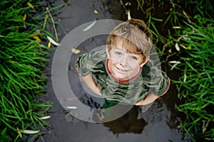 happy little school kids boy having fun walking through water in river in gum rubber boots. child portrait of healthy